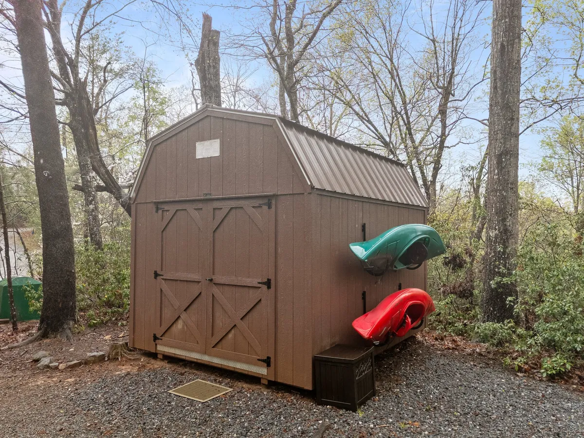 A cozy lakeside setup featuring a shed and brightly colored kayaks resting in the shade of surrounding trees. The image hints at sunny days spent launching kayaks and enjoying nature walks just steps from the cabin.