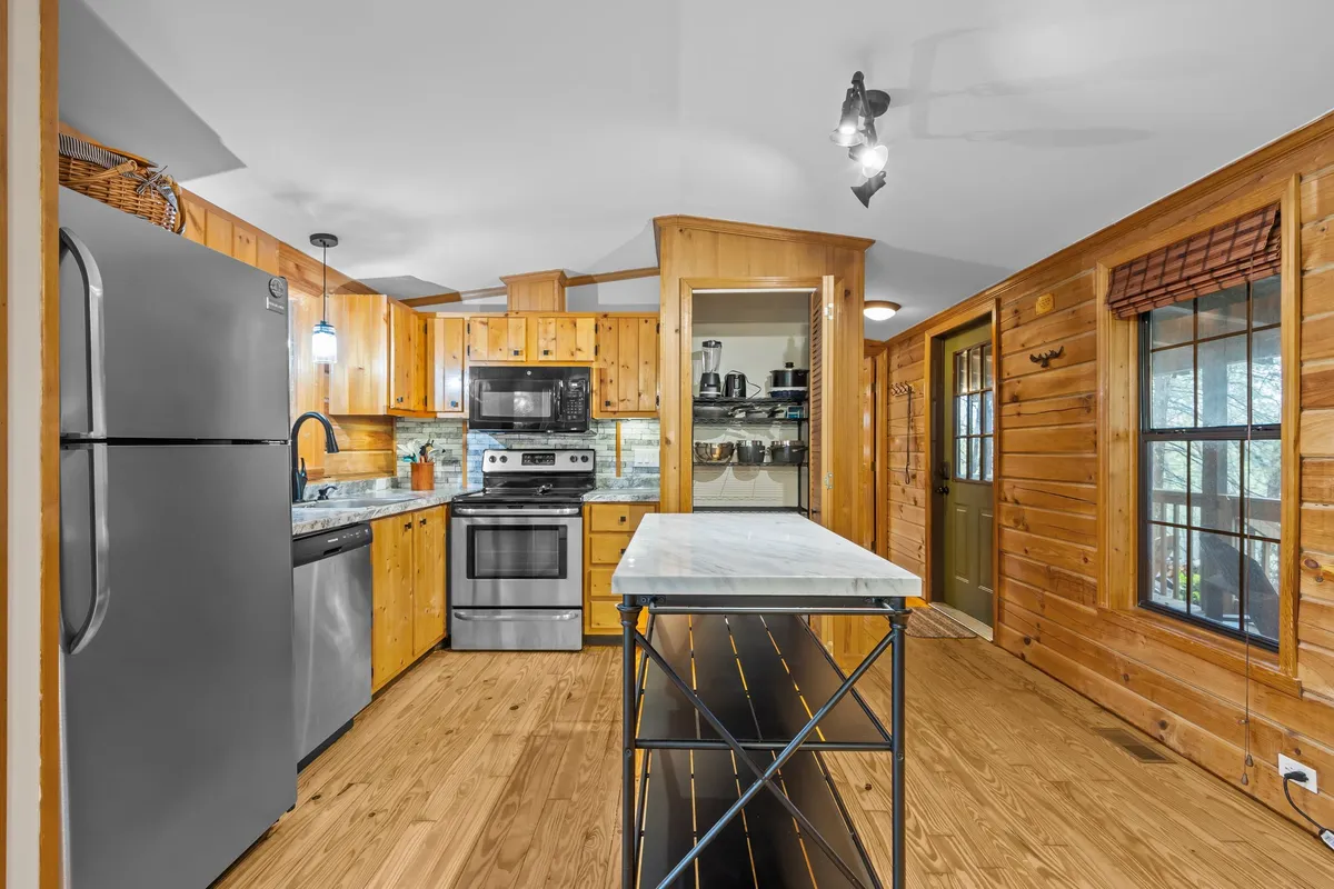 The photo showcases a kitchen with gleaming stainless steel appliances, rich wood cabinetry, and a marble island—a harmonious blend of updated function and cozy aesthetics. The inviting layout suggests a space ideal for both cooking and entertaining family or friends.