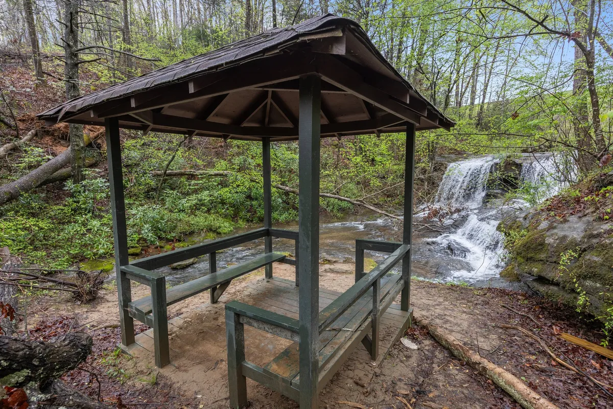 A charming gazebo nestles beside a cascading waterfall, surrounded by lush greenery. The setting invites relaxation and intimate moments, perfect for couples seeking quiet togetherness. The tranquil sound of falling water and the enchanting garden atmosphere enhance the mood of serenity.