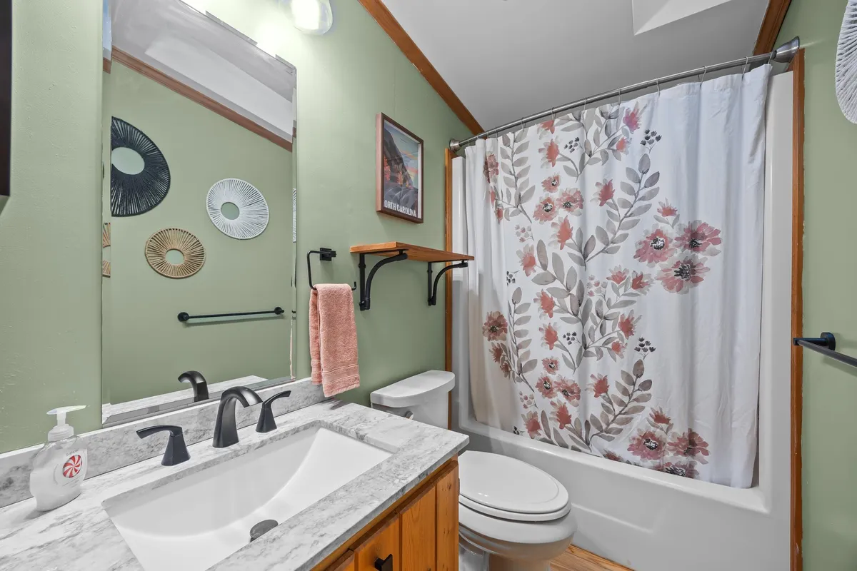A well-appointed bathroom with a marble countertop vanity, decorative floral shower curtain, and tasteful wall art. The space feels bright and calming, with thoughtful details for a relaxing experience.