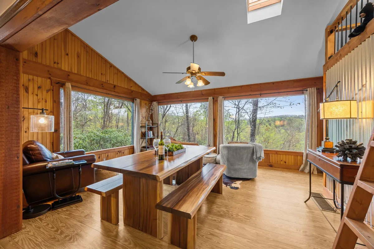 This interior image captures a large, rustic wooden dining table surrounded by comfortable seating and expansive windows that overlook lush greenery. The natural light bathes the dining area in warmth, creating a welcoming setting for group meals or quiet mornings.