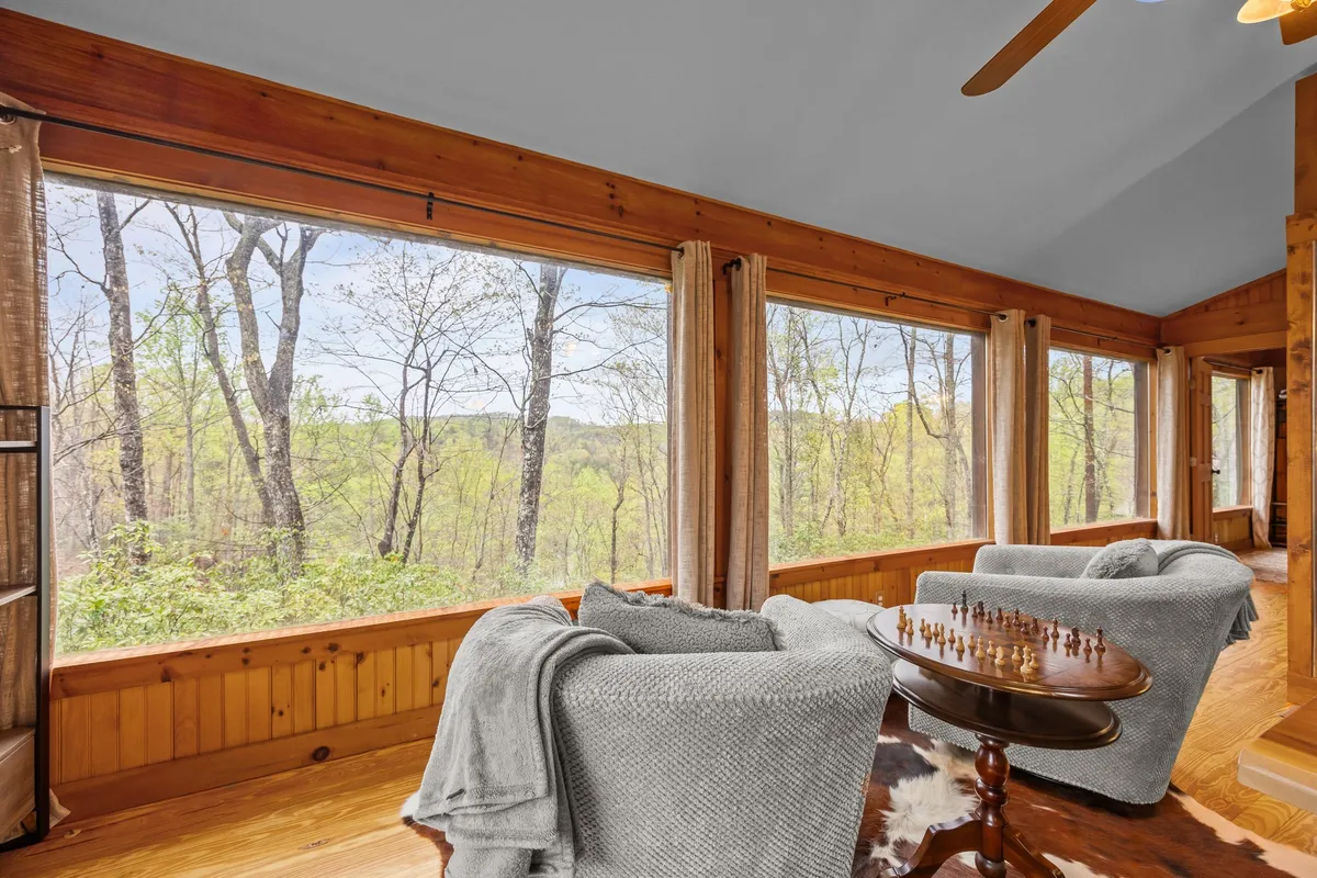 A tranquil corner with expansive windows overlooking a lush forest, a chess table set for play, and plush armchairs draped with throws. The peaceful ambiance and deep connection to the outdoors make this nook ideal for quiet moments, games, or simply soaking in the mountain scenery.