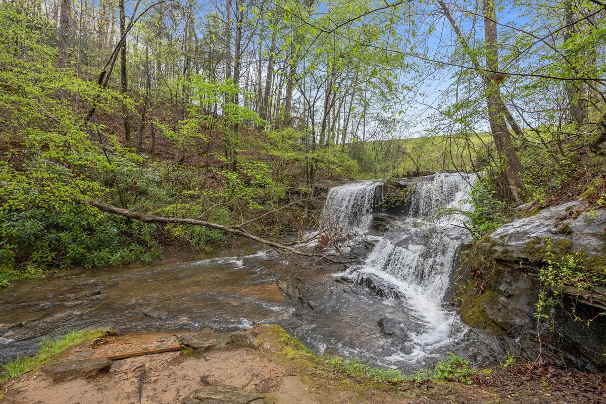 A tranquil scene of a waterfall cascading into a stream amid lush greenery and rocks, perfect for hiking, nature watching, and peaceful reflection in the great outdoors.