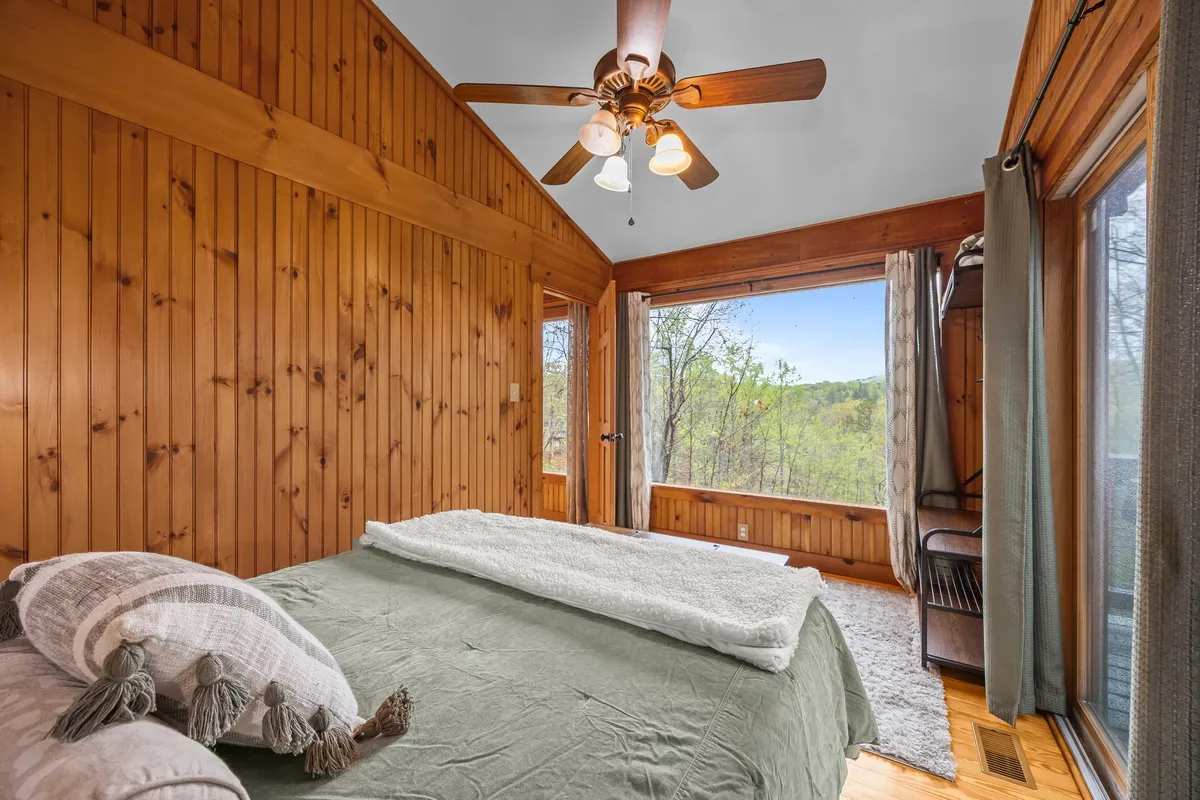 A tranquil bedroom with large windows offering sweeping nature views. The bed features soft textiles, and the inviting ambiance suggests moments of peace, such as reading by the window or waking up to the beauty of Lake Lure and the mountains.